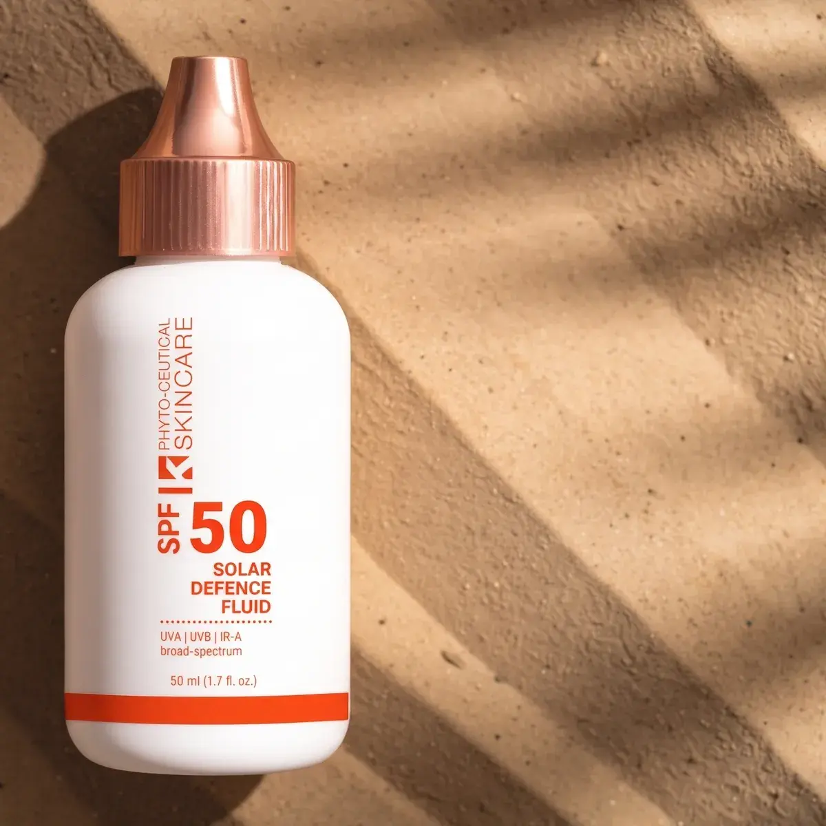 Solar Defence Fluid SPF 50 bottle lying on sand in dappled shade